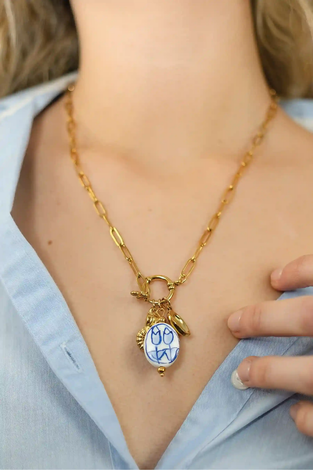 Gold necklace with a blue pendant worn by a person in a light blue shirt.