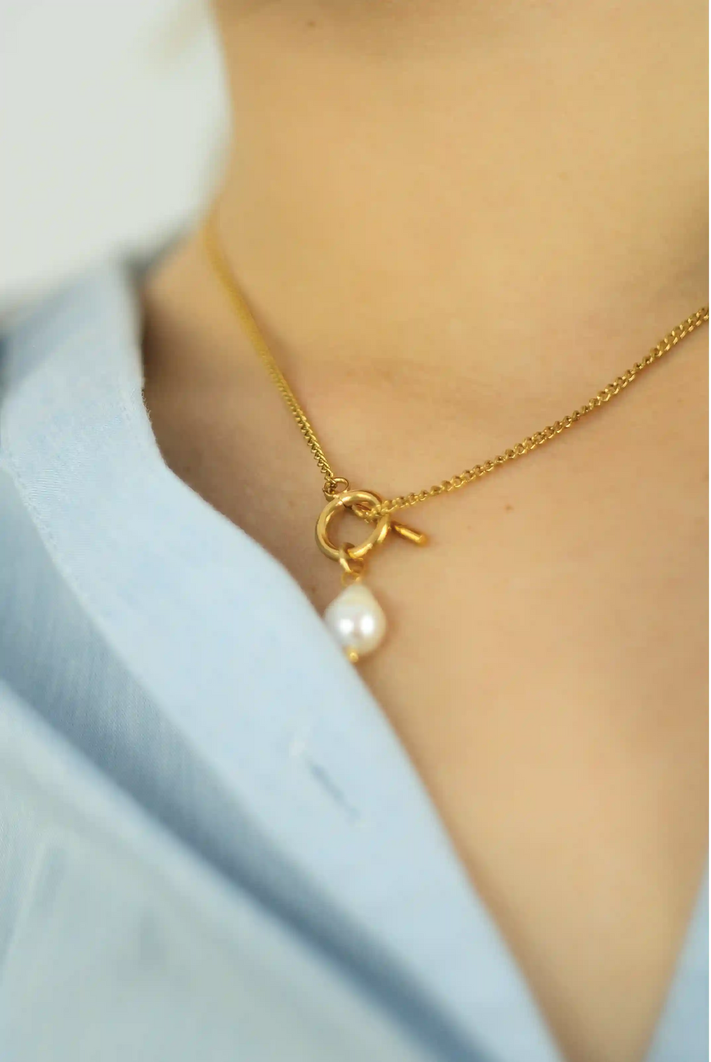 Gold necklace with a pearl pendant worn by a person against a light blue background
