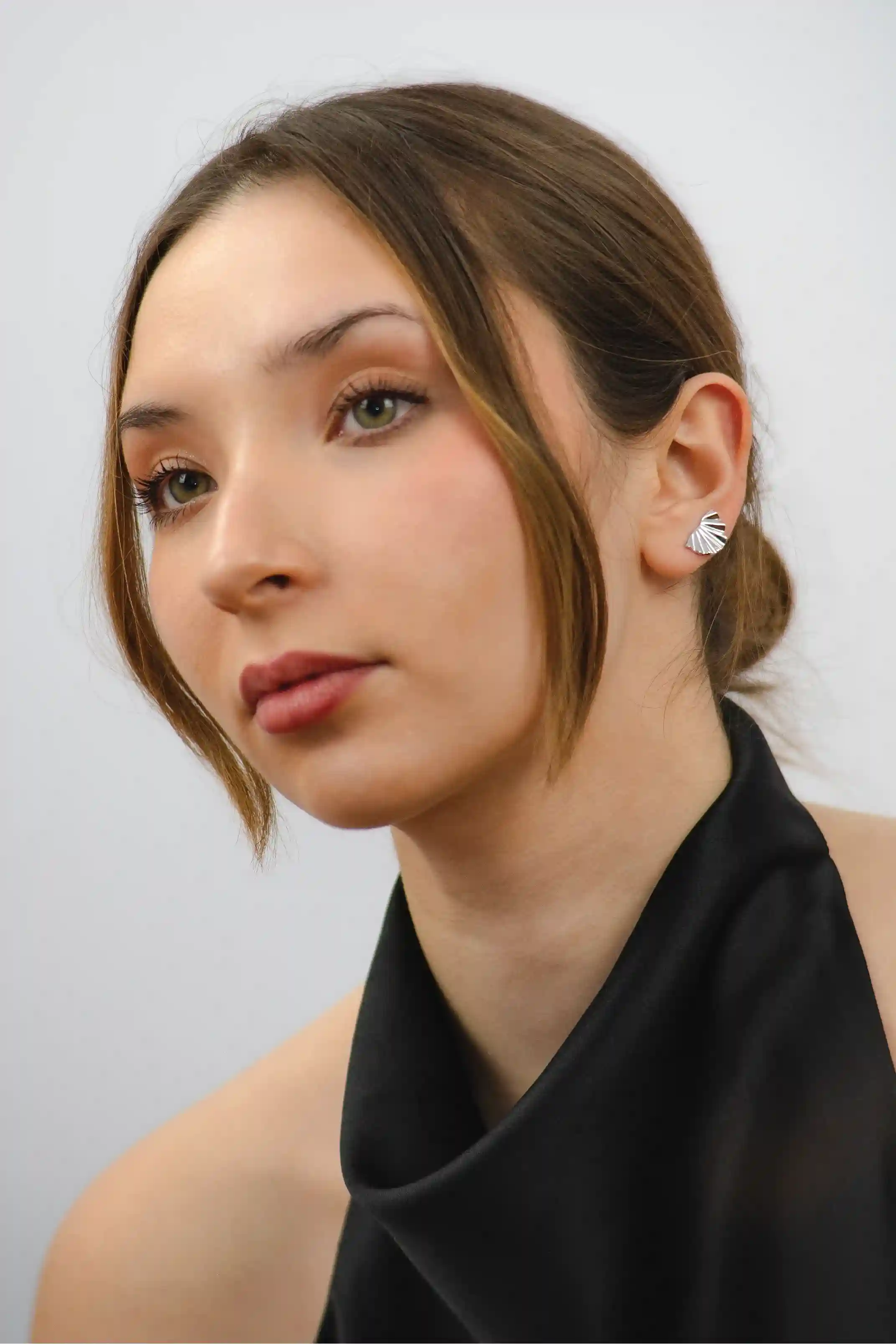 Close-up of a woman wearing a black top and silver earrings against a white background
