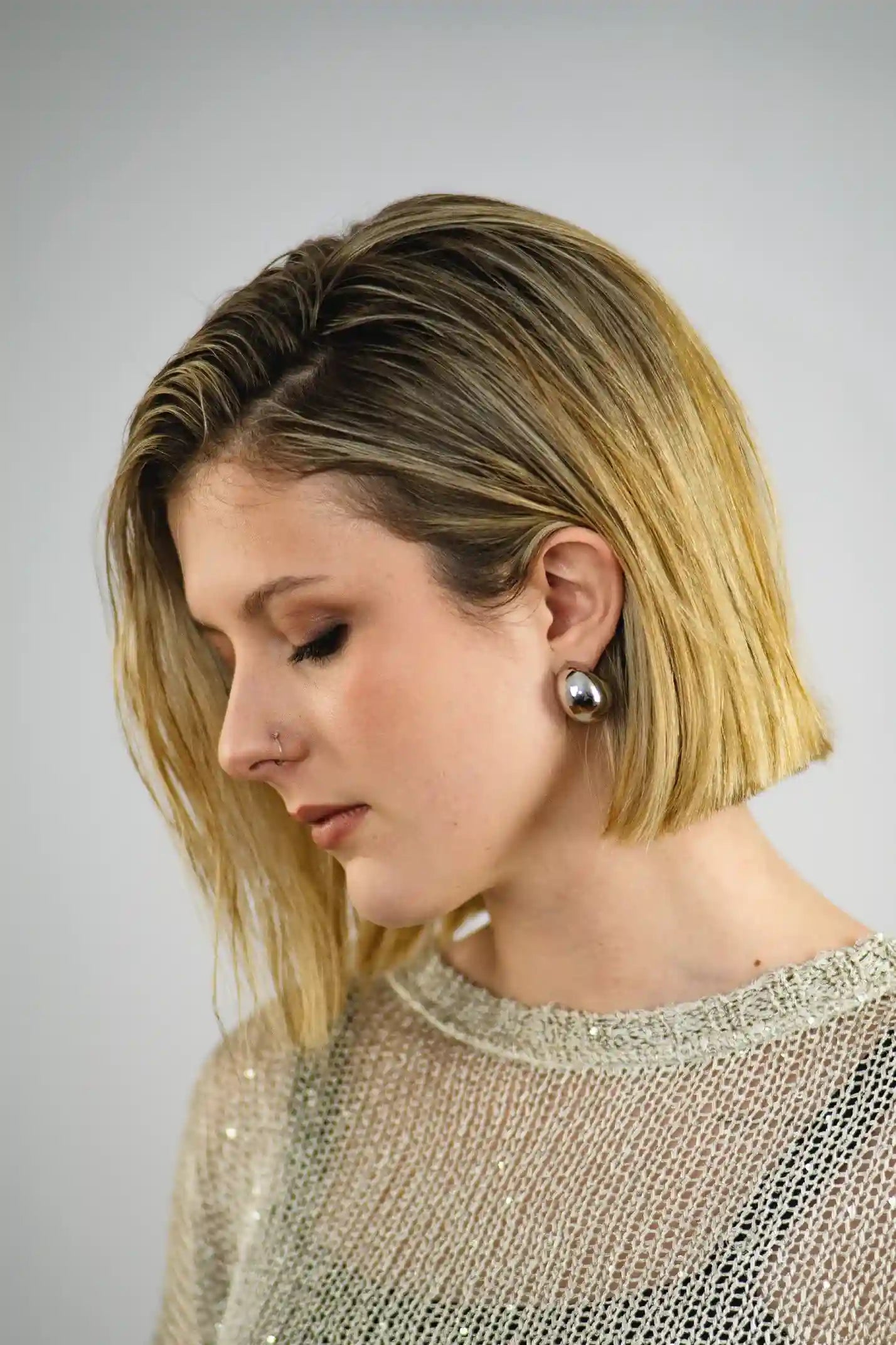 Woman with a short blonde bob haircut wearing a sparkly top against a plain background