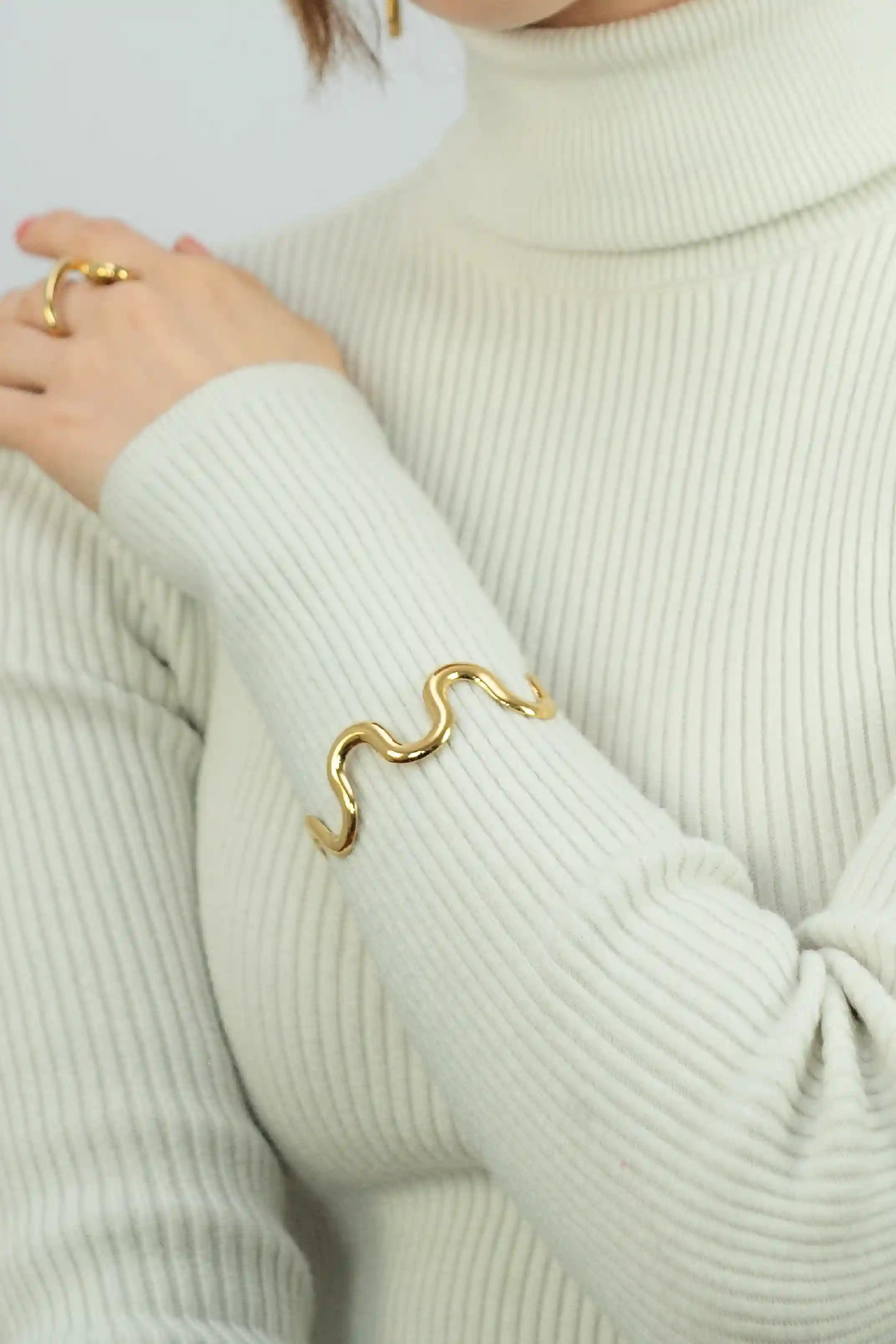 Person wearing a gold bracelet and ring on a light green sweater.