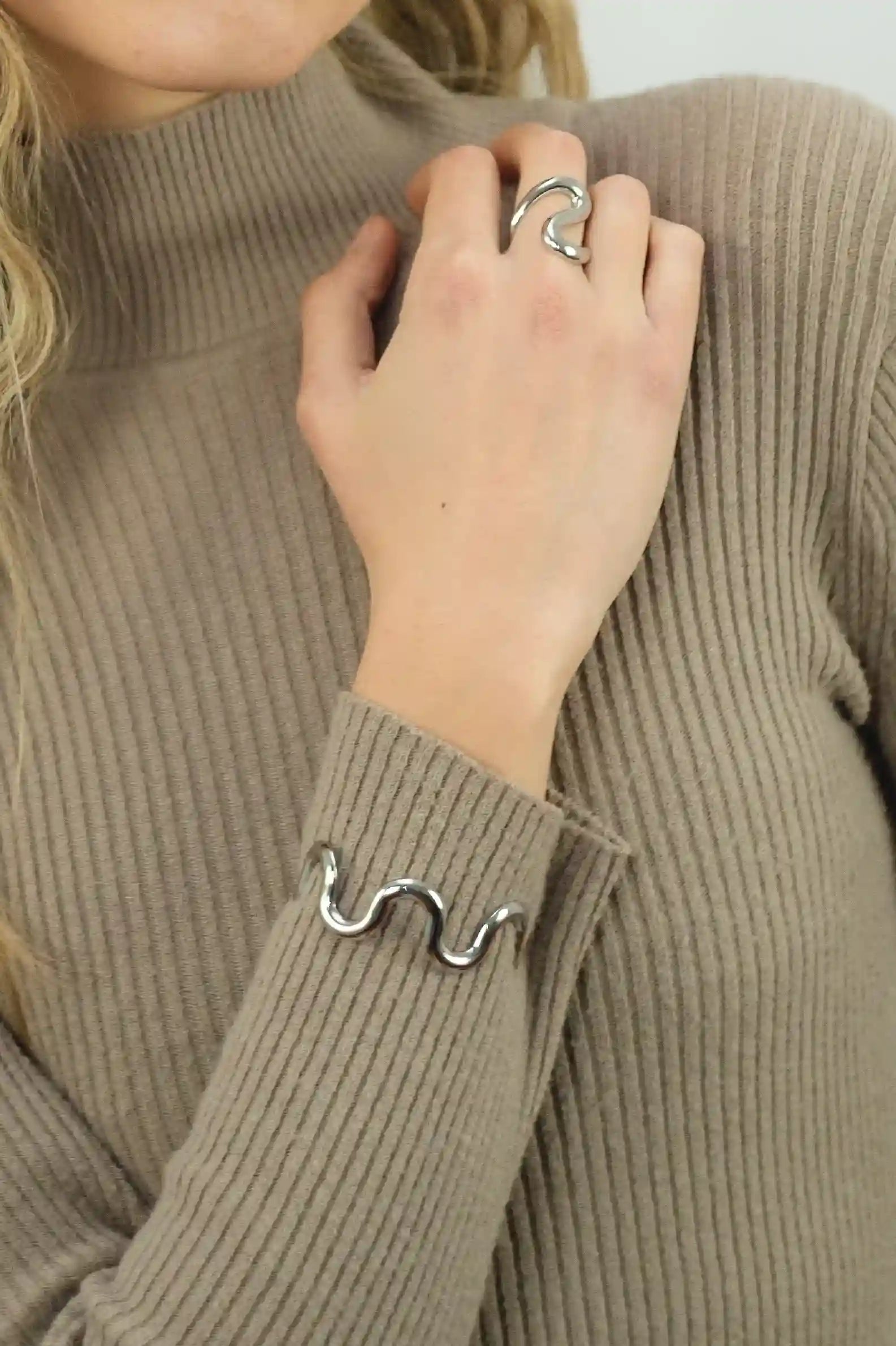 Person wearing a brown ribbed sweater with a metal ring on a finger.