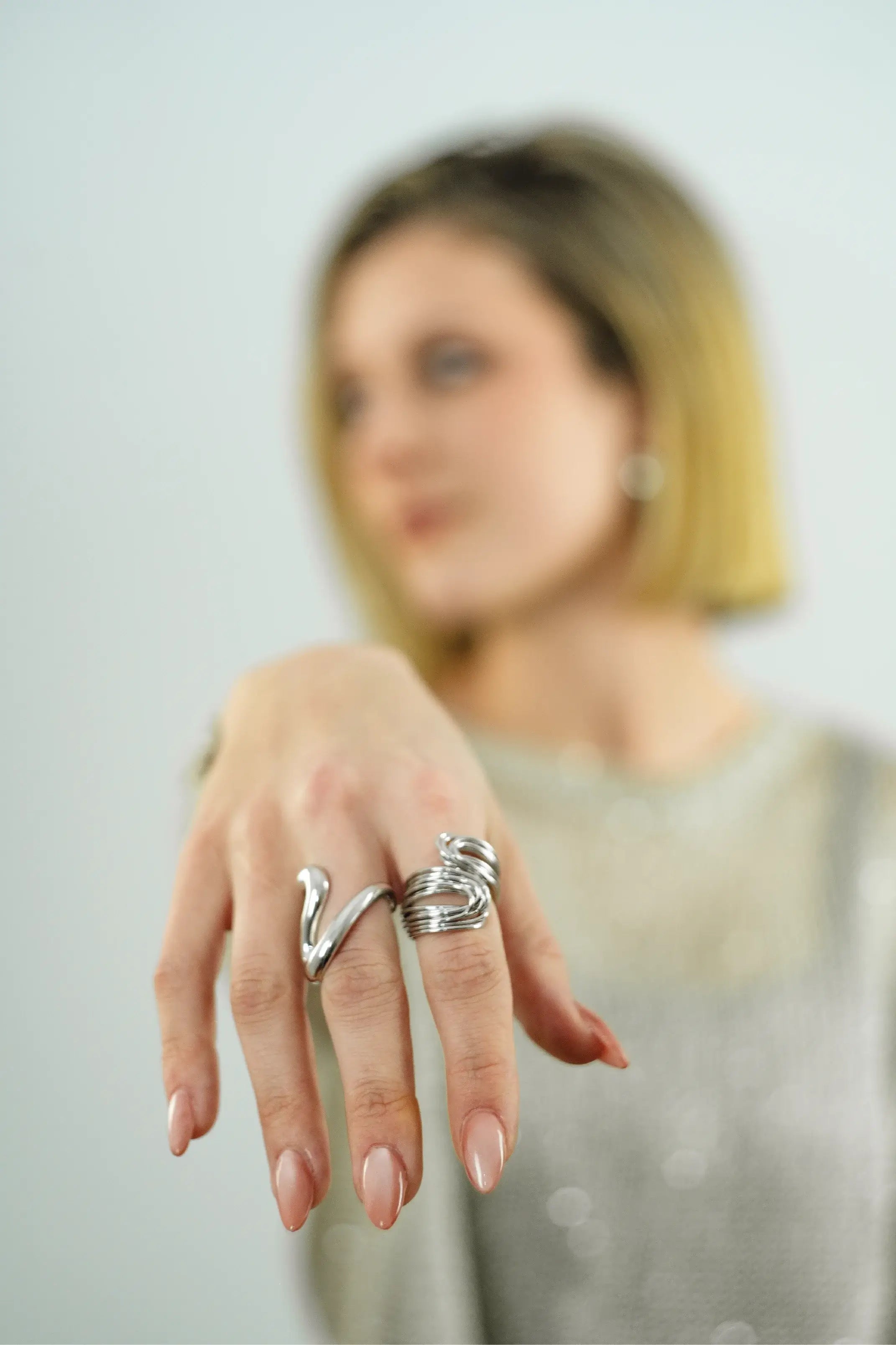 Close-up of a hand wearing multiple silver rings with a blurred background