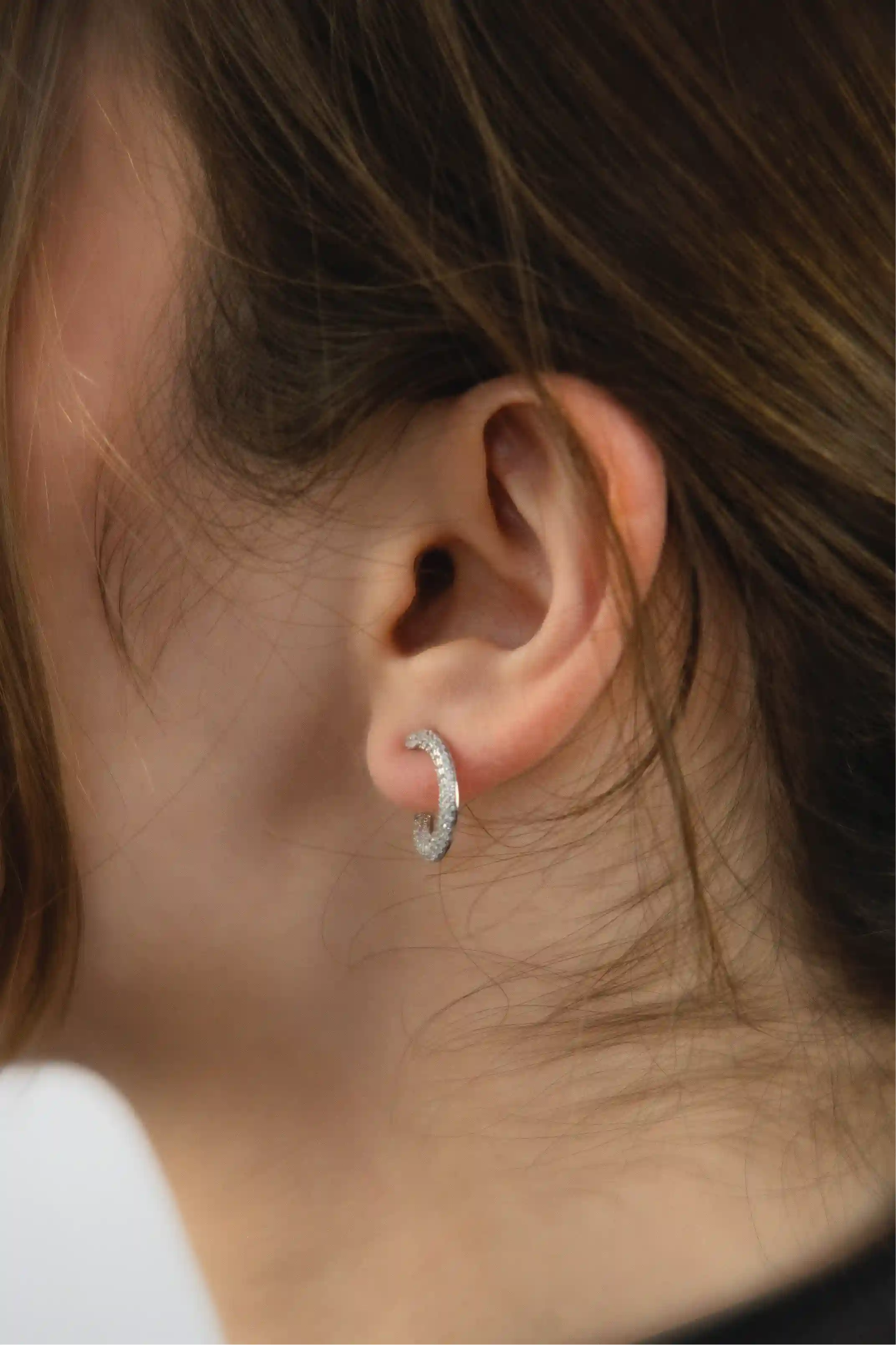 Close-up of an ear wearing a silver hoop earring with a blurred background