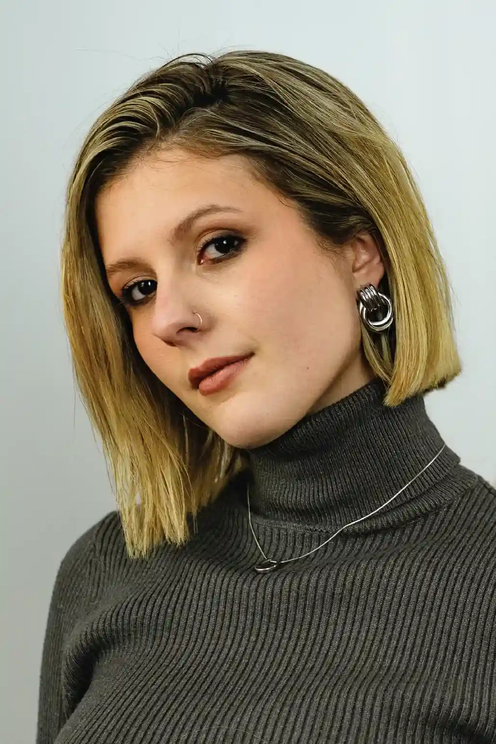 Woman with blonde hair wearing a gray turtleneck against a light background