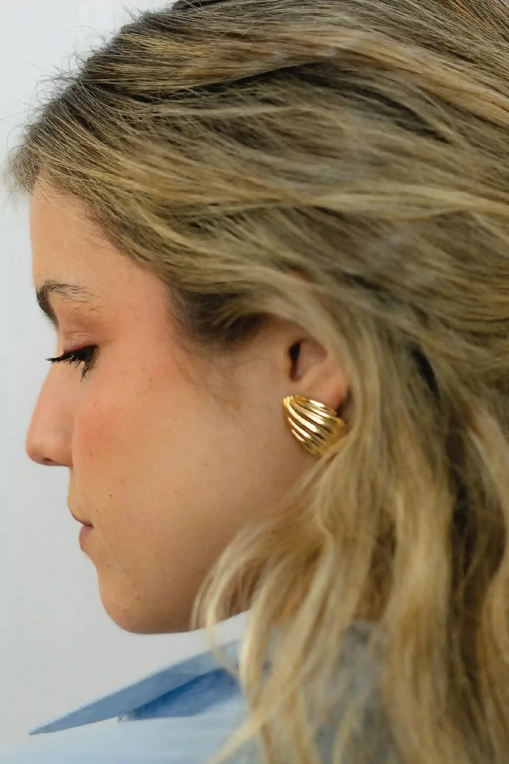 Close-up of a person wearing gold shell-shaped earrings with a neutral background