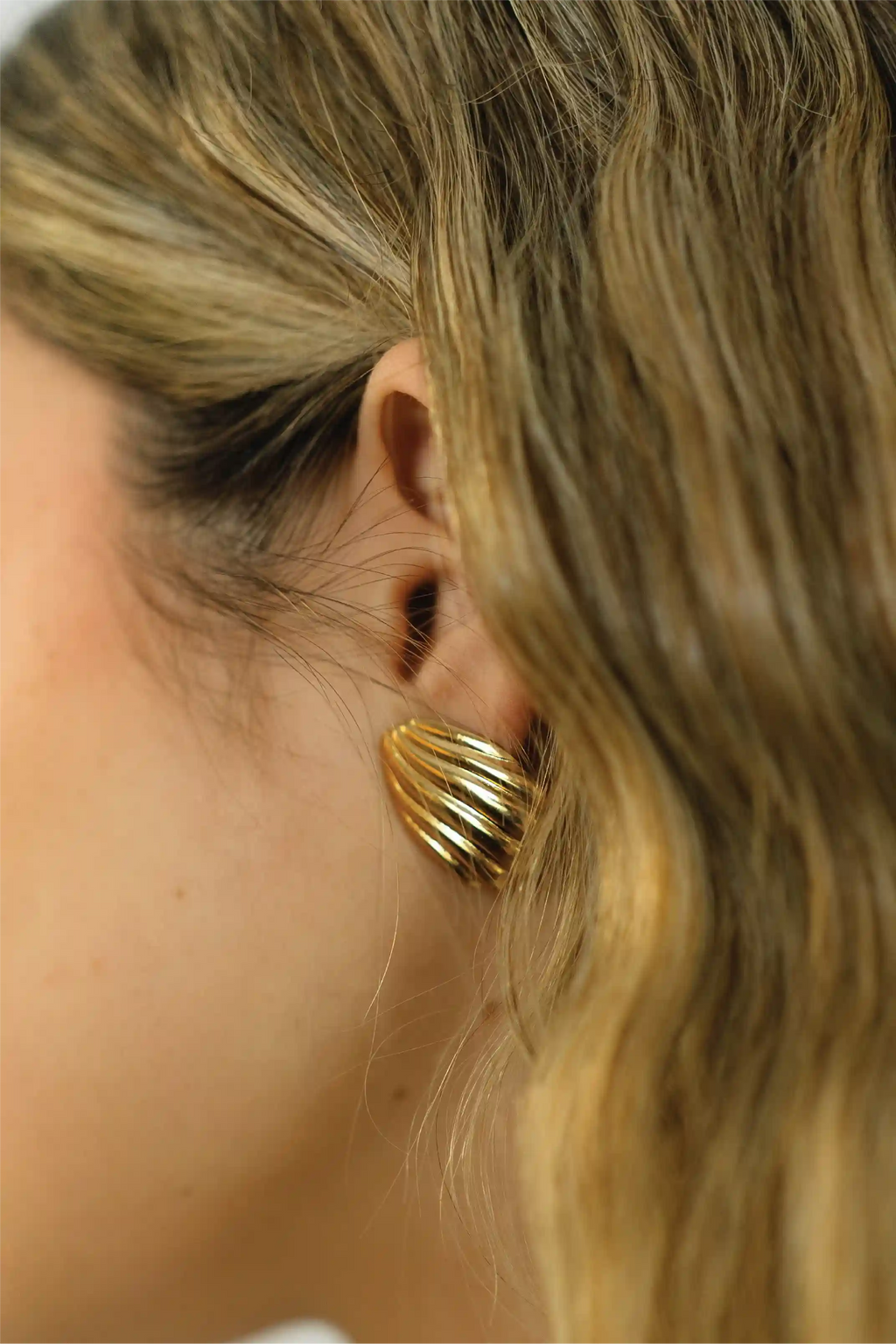 Close-up of a person wearing a gold earring with blonde hair.