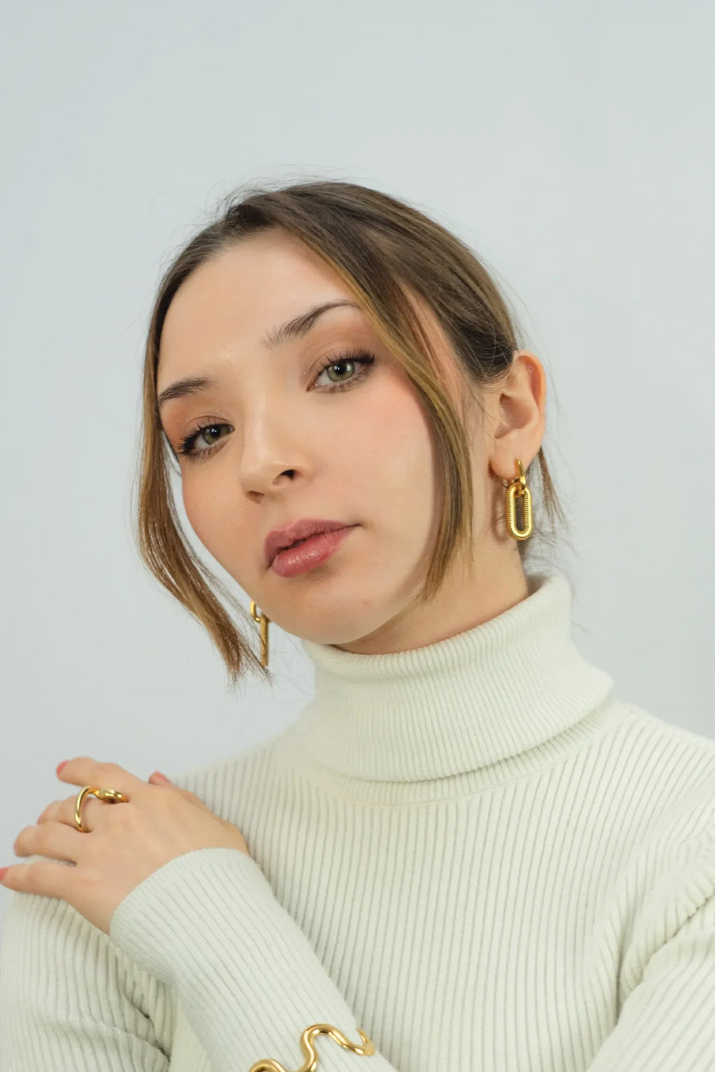 Woman wearing gold earrings and a ring against a light background