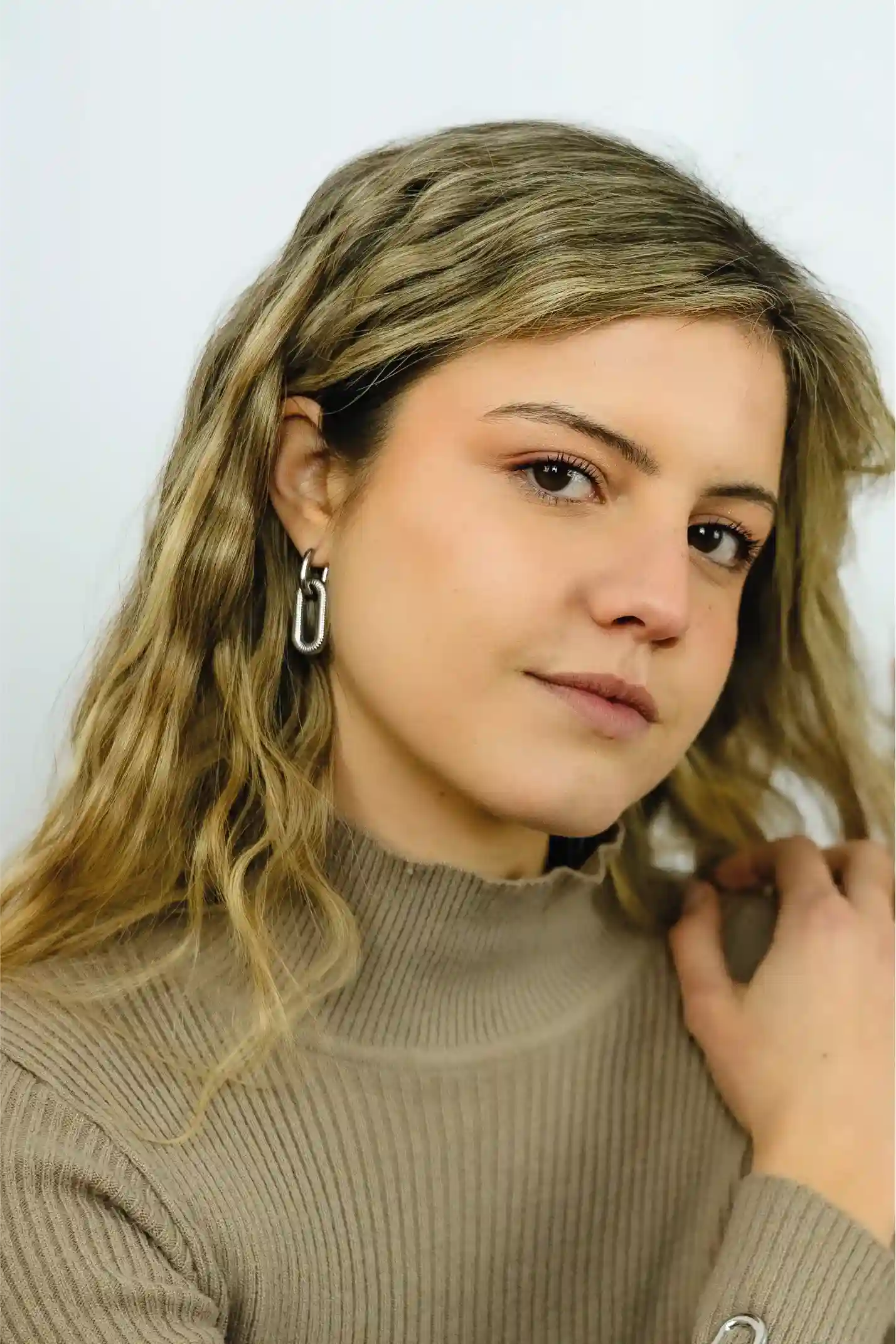 Woman with blonde hair wearing a beige sweater against a white background
