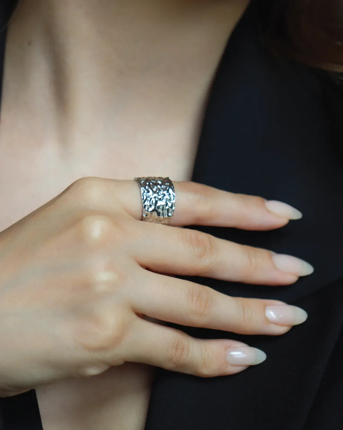 Close-up of a hand wearing a silver ring with intricate design on a dark background
