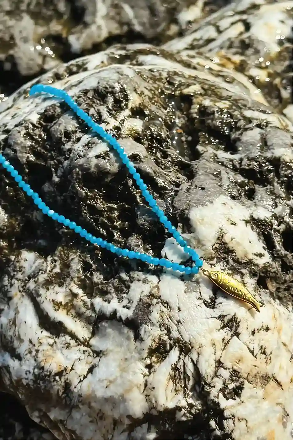 Blue beaded necklace with a gold clasp on a textured rock surface