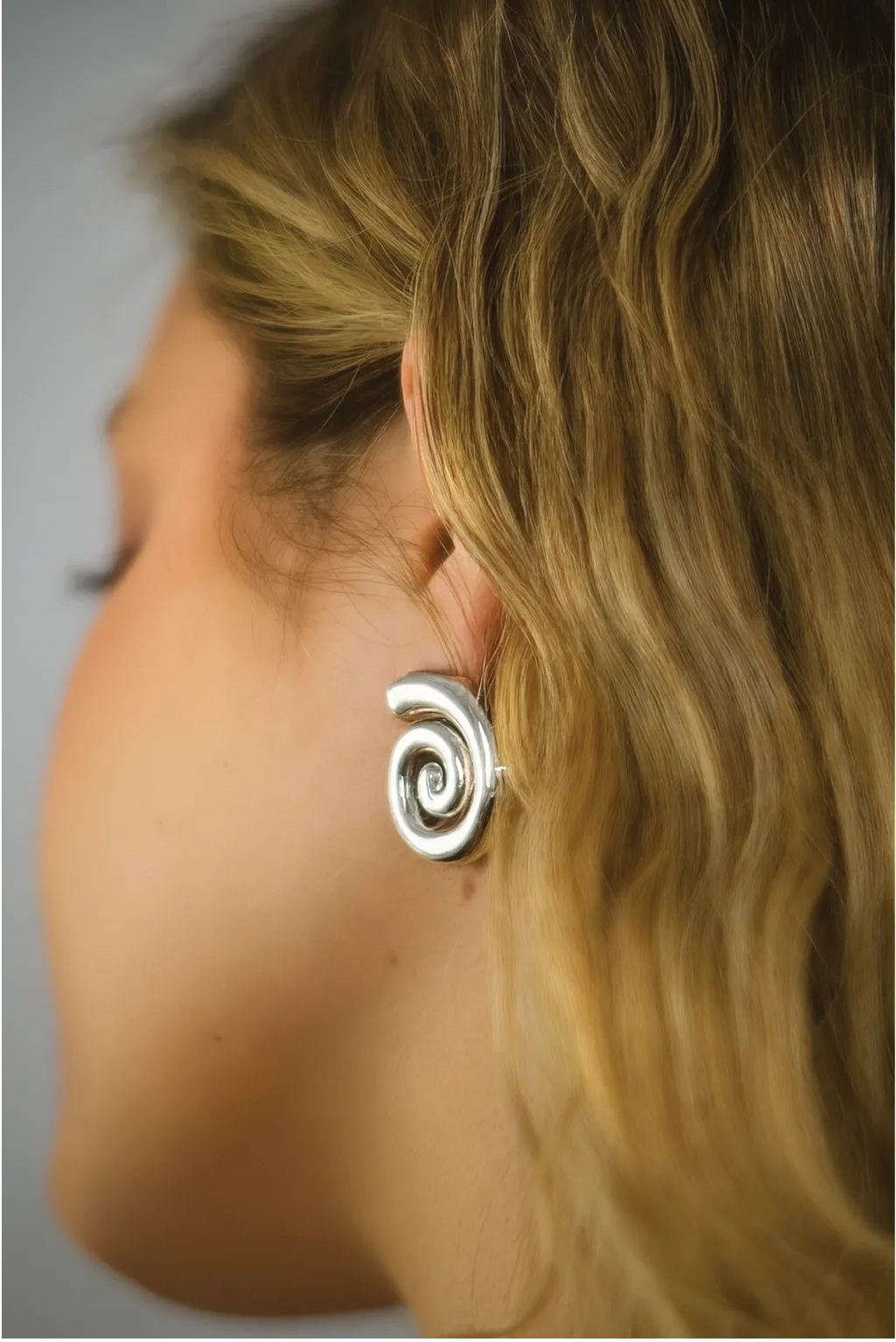 Silver spiral earring worn by a person with blonde hair.